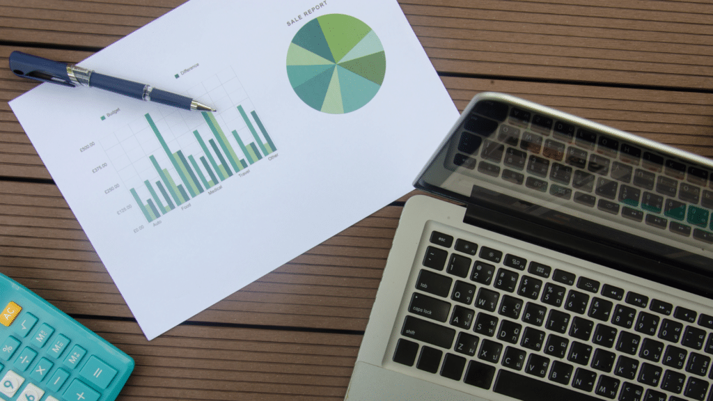 An image of a desktop with a laptop, calculator and document with a graph on it.